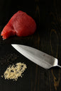 Raw tuna steak with a knife and seasoning on a dark surface
