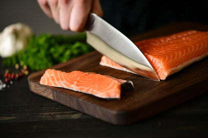 Person cutting a piece of salmon on a wooden board with a knife.