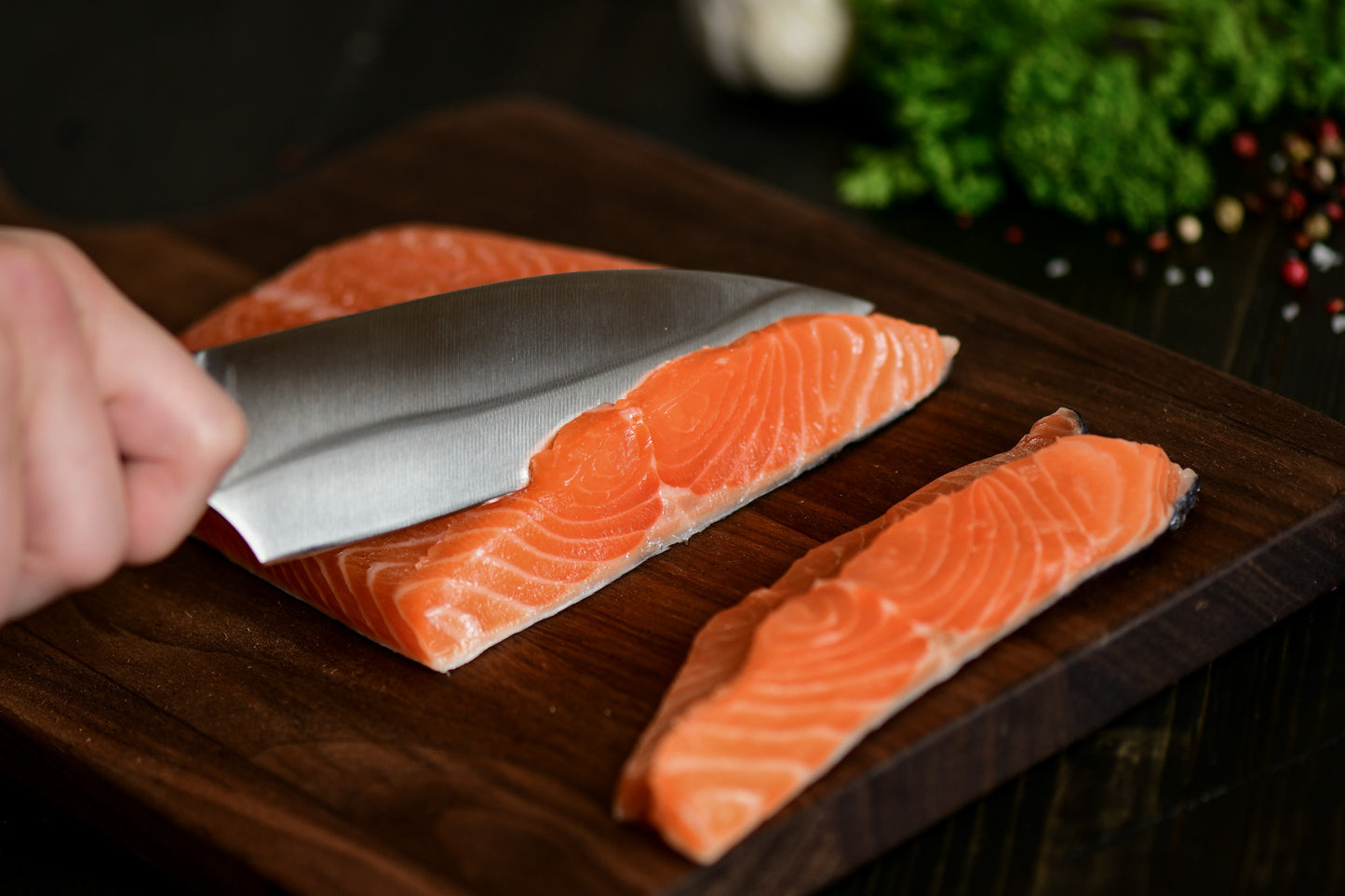 Person cutting salmon fillets on a wooden board with a knife.