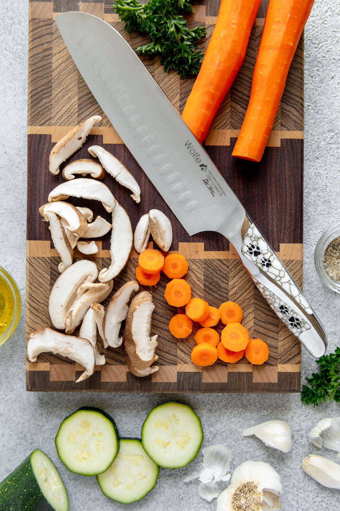 Wooden cutting board with sliced mushrooms, carrots, and a chef's knife on a gray surface.
