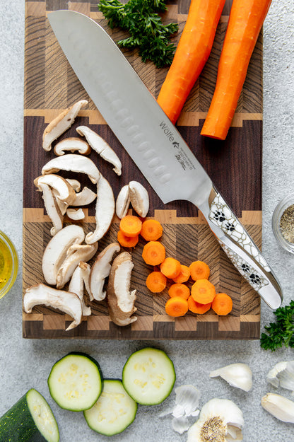 Wooden cutting board with sliced mushrooms, carrots, and a chef's knife on a gray surface.