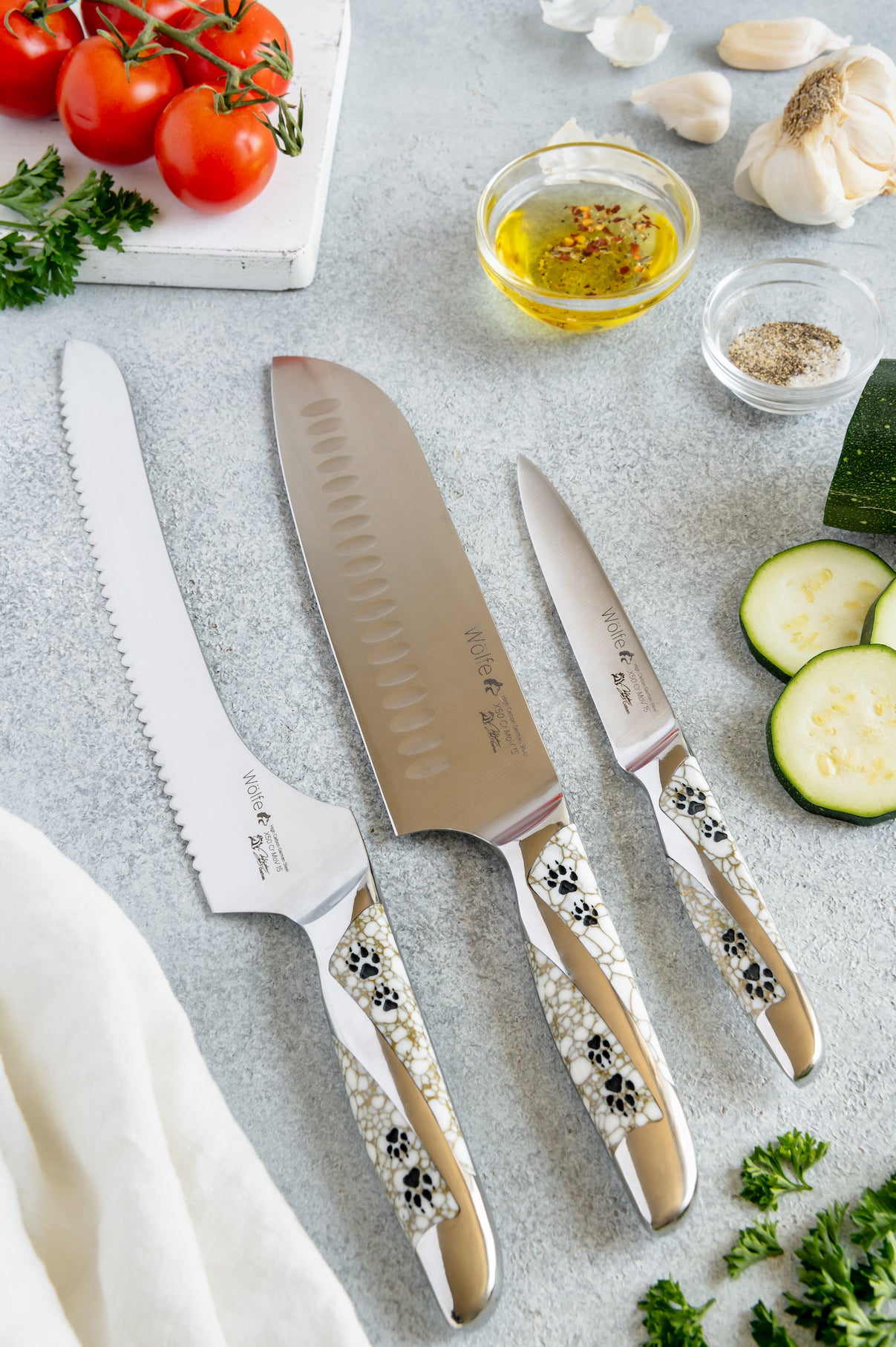 Set of knives with decorative handles on a kitchen counter with vegetables and oil.