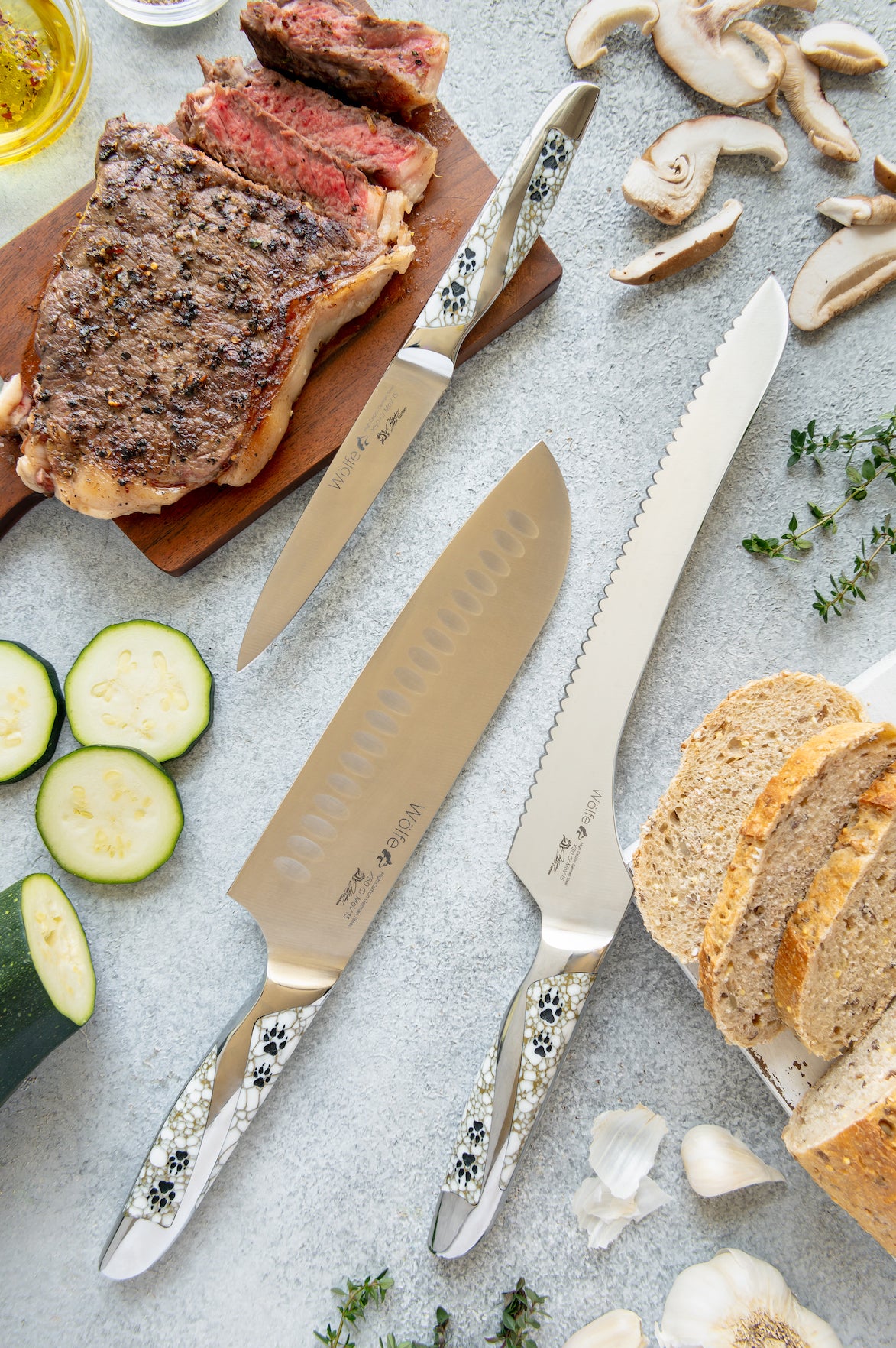 Steak with sliced bread, vegetables, and knives on a gray surface