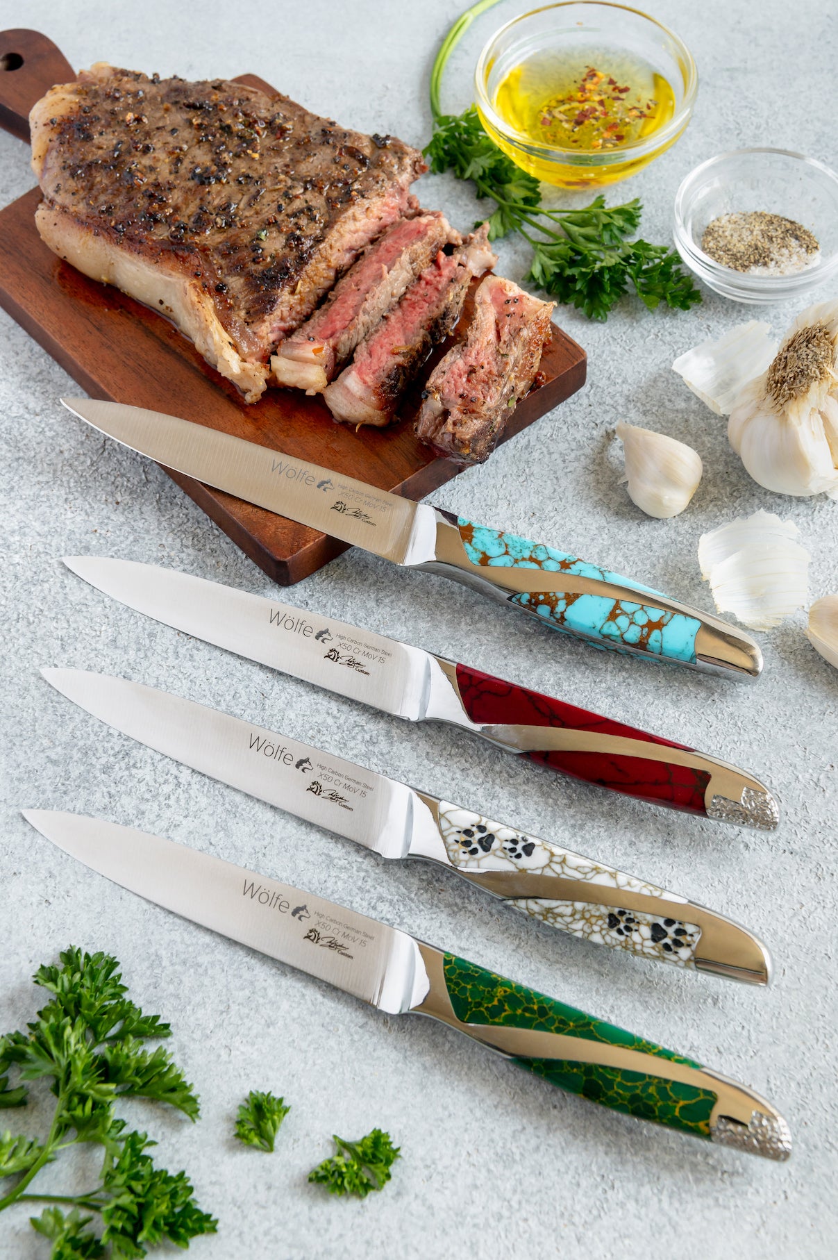Set of steak knives with decorative handles on a table with sliced steak and herbs.